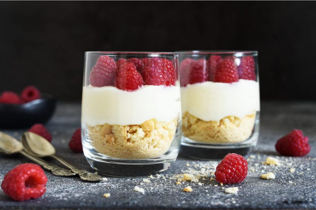 Käsekuchen im Glas mit Himbeeren und Butterkeksen
