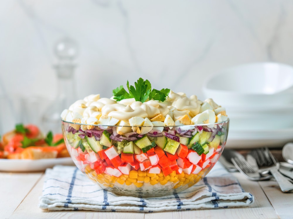 Schichtsalat mit Krabbenstäbchen, Mais, Gurken und Eiern